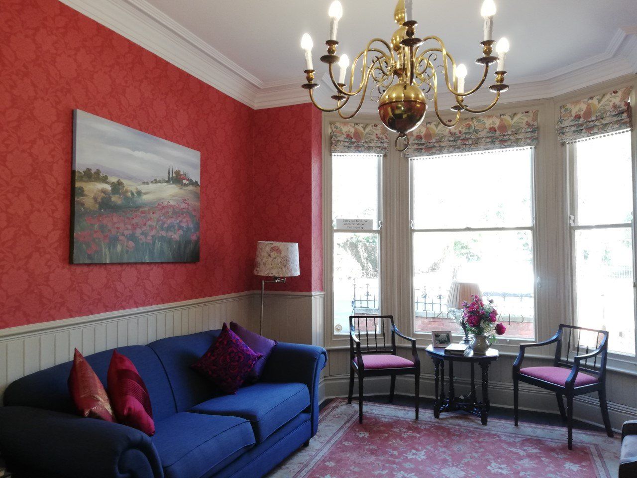 The sitting room, with red damask walls, a chandelier and a bay window