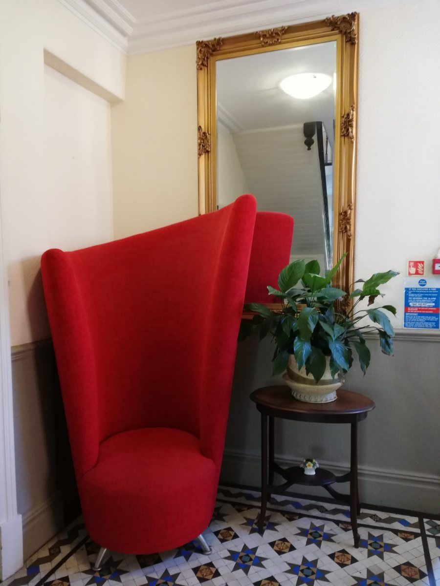 A red wingback chair beside a gilded mirror in the hallway