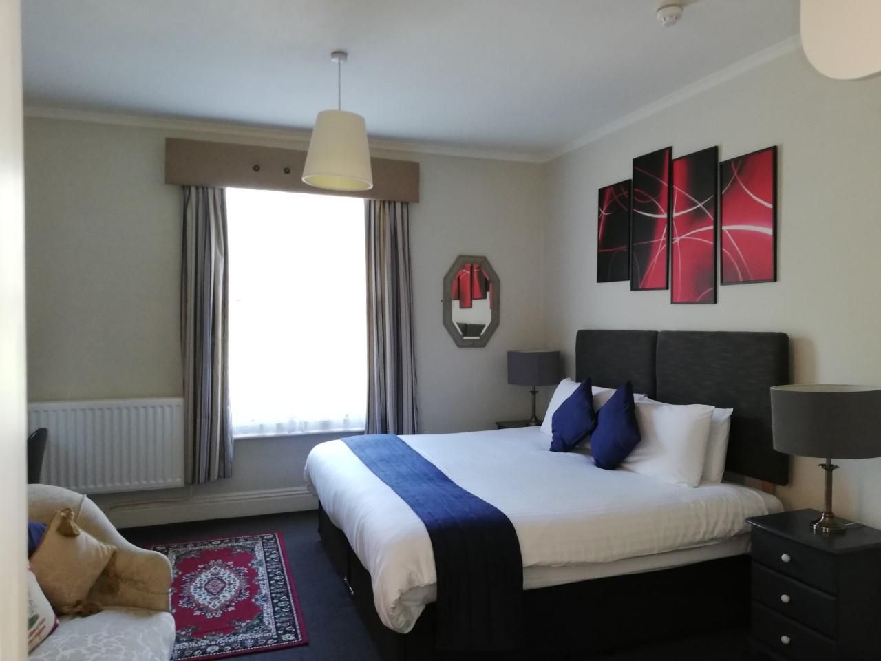 A double room with navy and white bedding beneath red abstract art